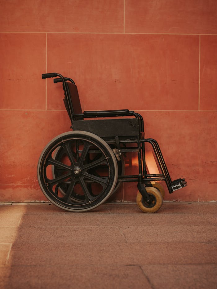 A black wheelchair stands against a striking red wall, highlighting urban accessibility themes.