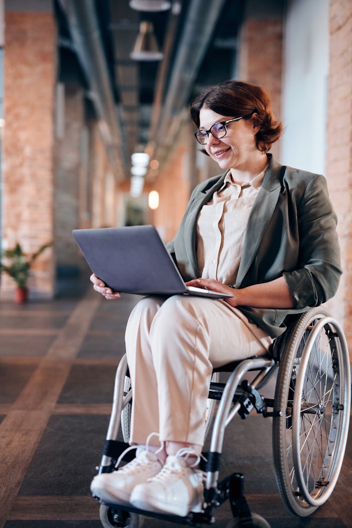 Smiling businesswoman in a wheelchair working on a laptop in modern office.